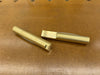 Two brass bench dogs placed on a brown textured workbench surface.