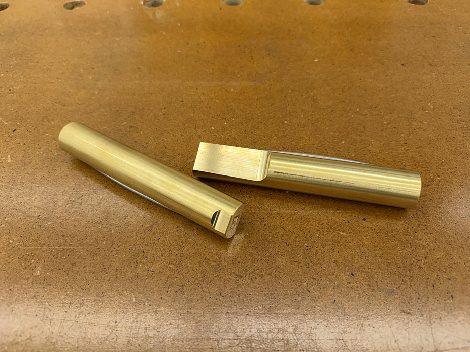 Two brass bench dogs placed on a brown textured workbench surface.