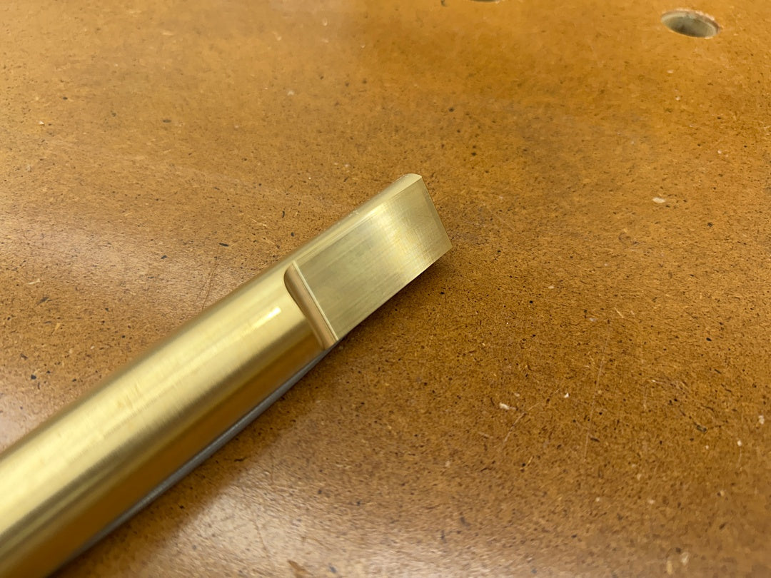 A close-up of a Rob Cosman 1-inch brass bench dog resting on a brown wood surface.