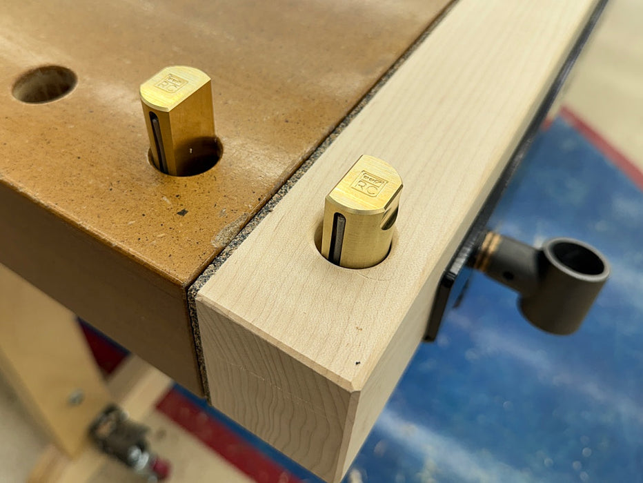 Close-up of a two Rob Cosman Brass 1-inch diameter bench dogs in a workbench dog holes.