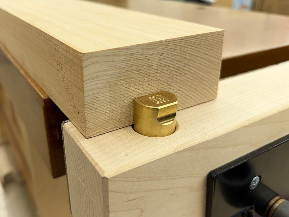 Close-up of a lRob Cosman 1-inch brass bench dog holding a piece of wood with its primary face.