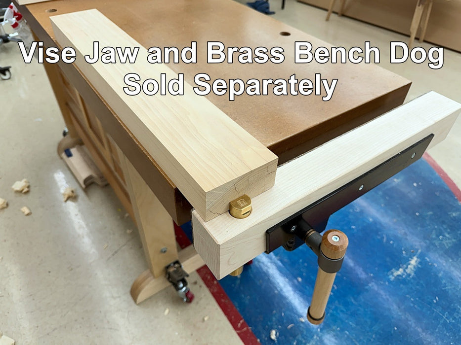 A close-up of a wooden bench vise with a brass adjustment nut and a wooden handle, mounted on a wooden workbench in a workshop. White text overlay reads 'Vise Jaw and Brass Bench Dog Sold Separately'.